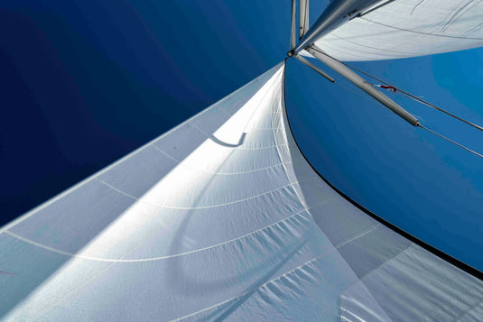 Vue en contre-plongée du gréement d'un voilier léger, montrant le mât, les haubans et les voiles blanches gonflées par le vent.