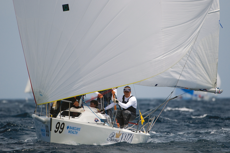 Voilier de course Princesa Yaiza sous spinnaker blanc, équipage en action, logo Barclays Wealth visible, mer légèrement agitée, autres voiliers au loin.