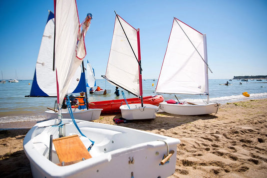Plusieurs dériveurs et catamarans de sport sur une plage, illustrant les équipements de voile légère spécialisés proposés par Yachting Thommeret.