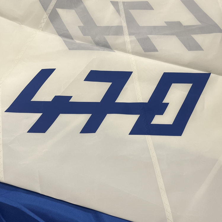 Laden Sie das Bild in Galerie -Viewer, Détail de la grand voile de dériveur 470 avec le logo de classe 470 en bleu collé sur la voile blanche en dacron.
