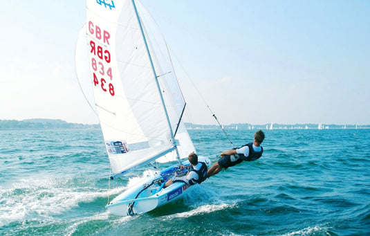 Deux marins sur un dériveur blanc et bleu avec des voiles blanches et rouges sur l'eau bleue